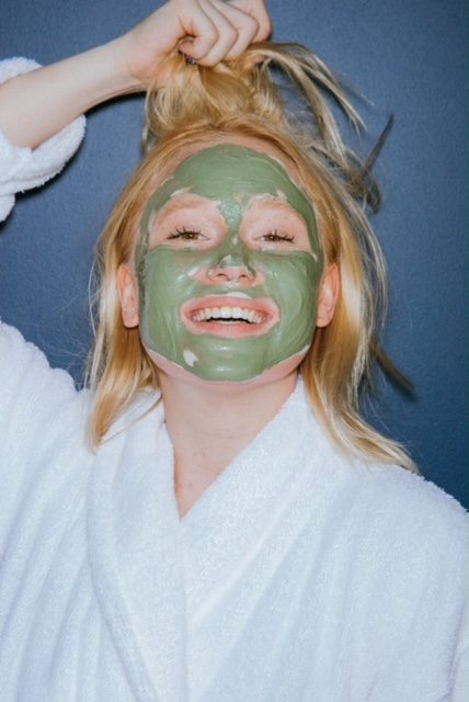A woman in a bathrobe with a green clay mask on her face.