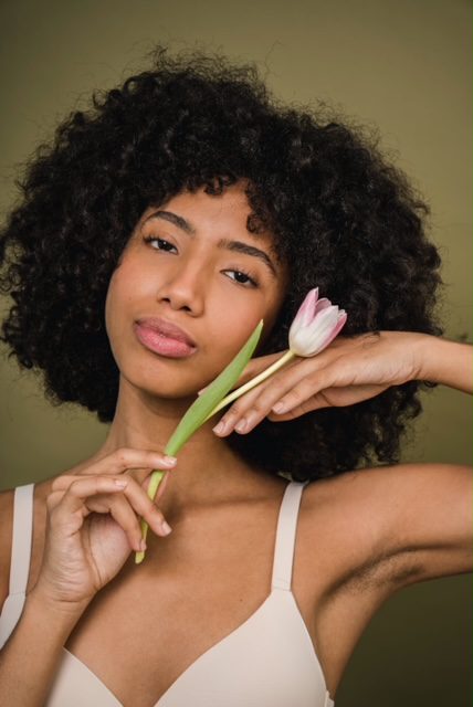 A black woman with natural makeup holding a tulip in her hand.