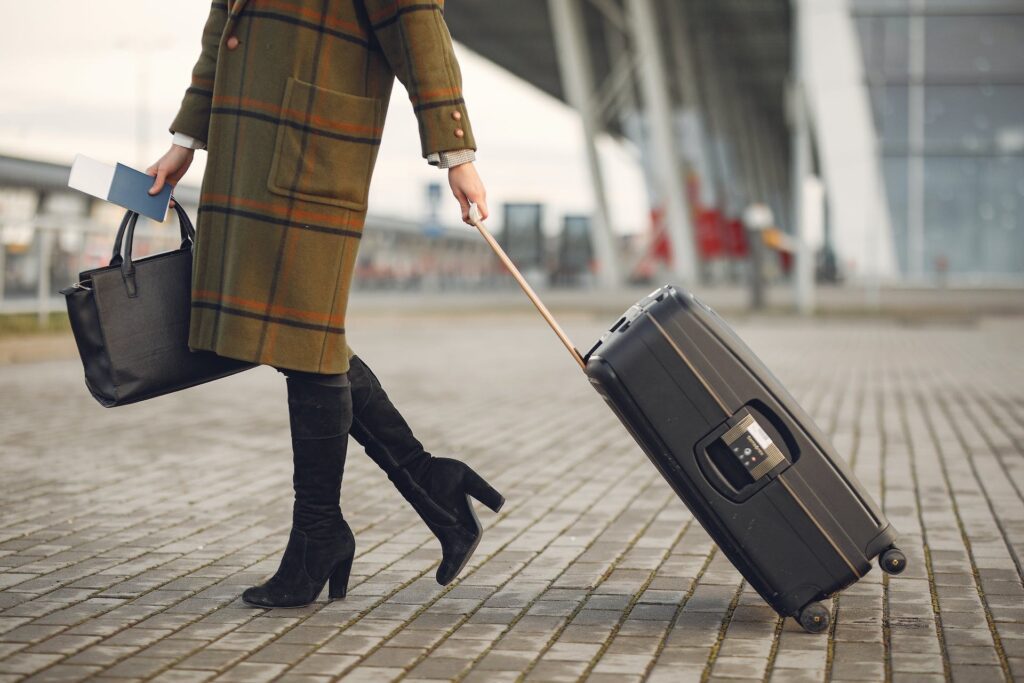 A woman in a coat and boots is pulling a suitcase.