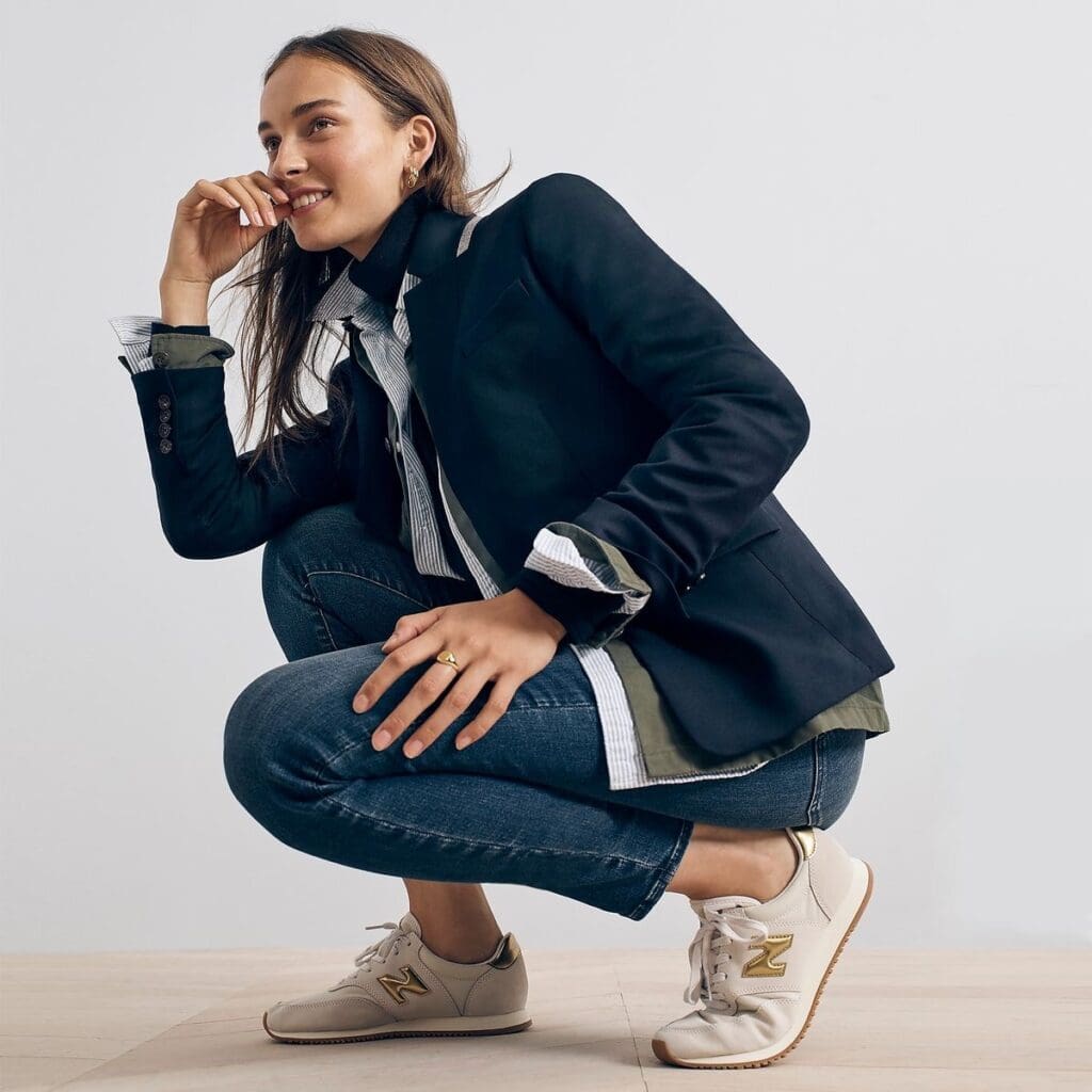 Woman in a J Crew blazer and jeans squatting with a smile, showcasing the J Crew ThredUp resale program.