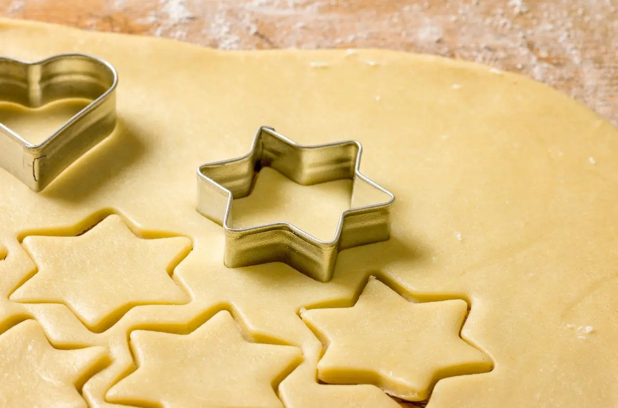 Rolling dough with star-shaped cookie cutters on a wooden surface.