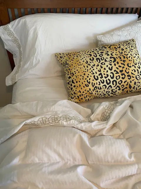 An unmade bed with white bedding and a leopard print pillow.