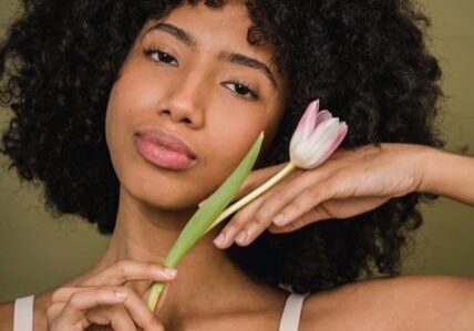 A black woman with natural makeup holding a tulip in her hand.