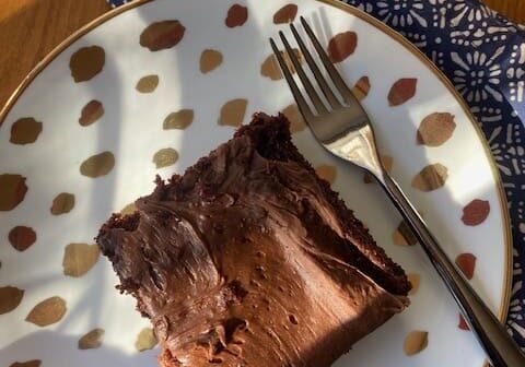 A slice of family recipes chocolate Waldorf cake on a patterned plate with a fork, on a wooden table with a blue napkin.